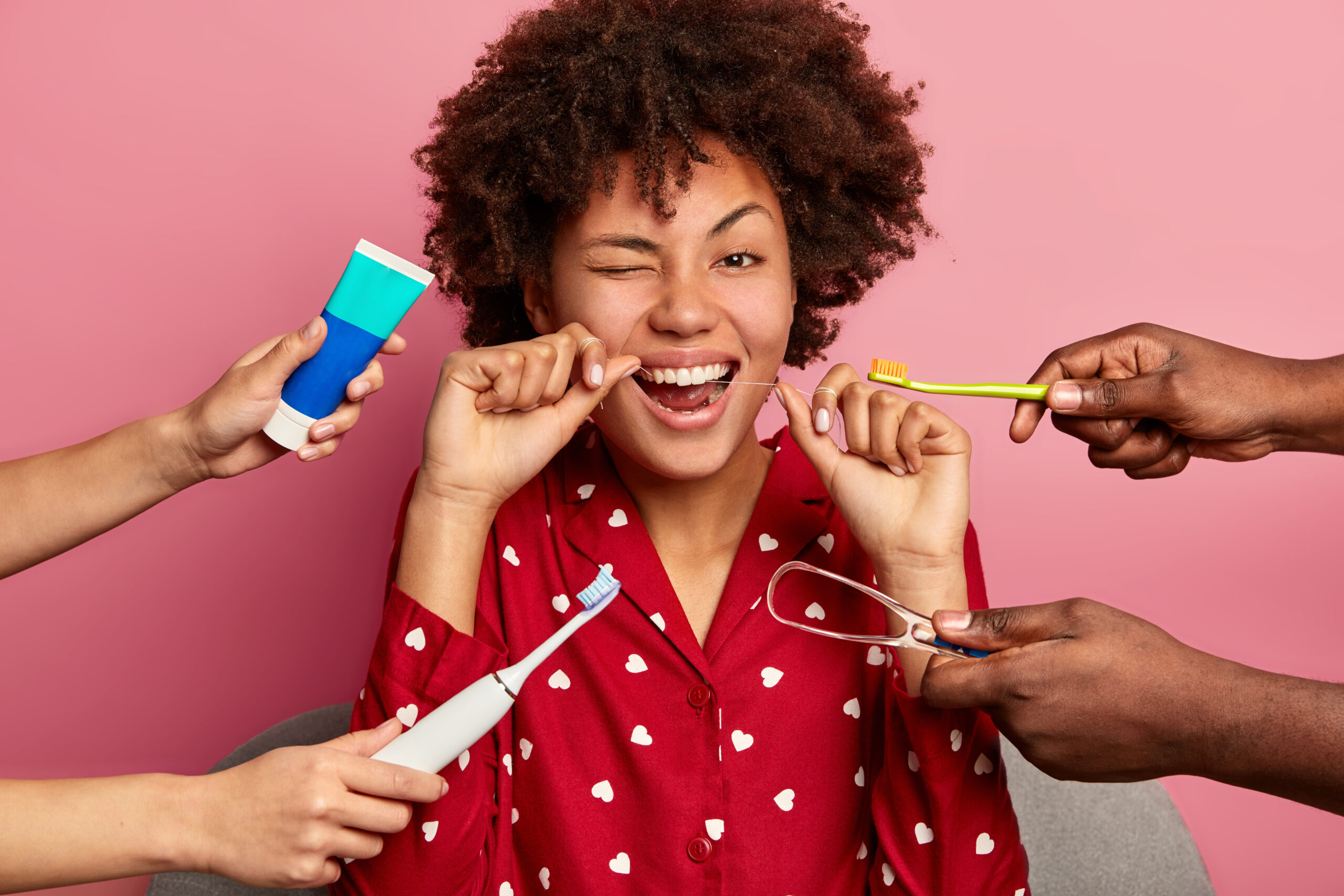 happy curly young woman brushes teeth with tooth floss cares about oral hygiene surrounded with toothpaste electric toothbrush tongue cleaner scaled 1