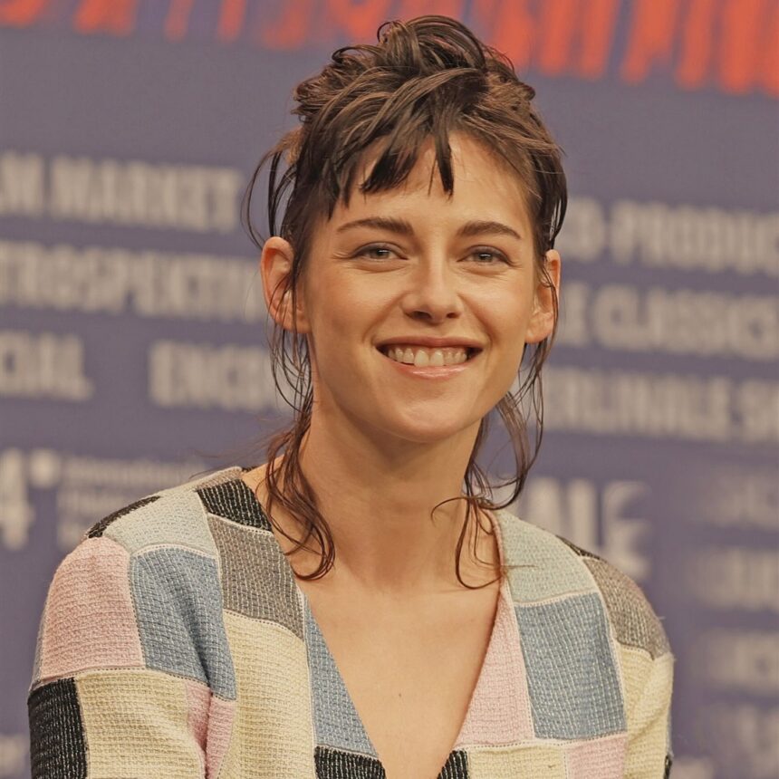 Kristen Stewart sorri durante coletiva de imprensa, com blusa de tricô colorida